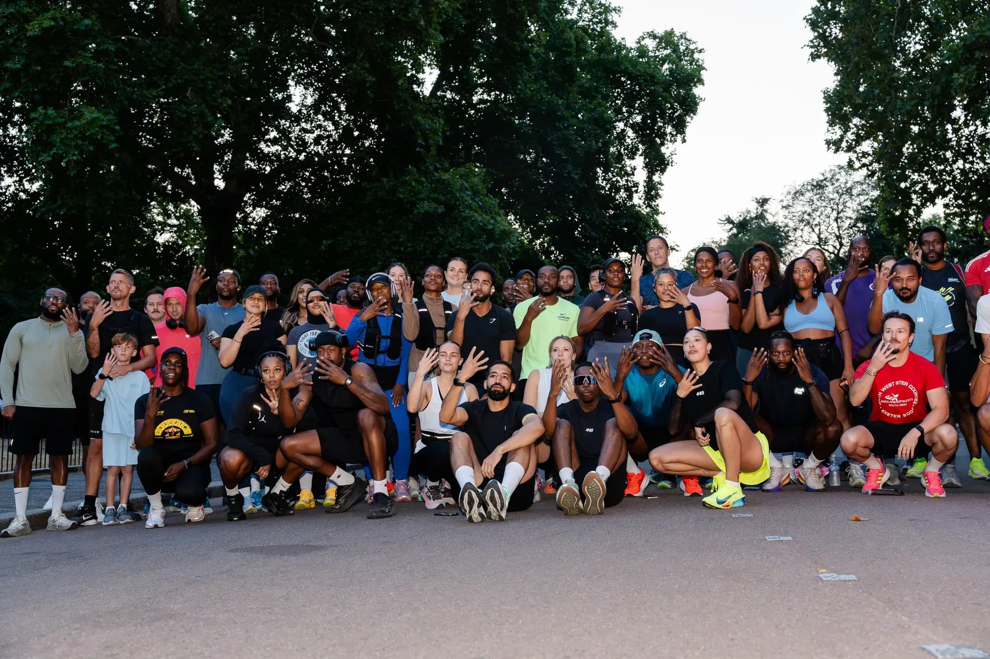 The full 445 Crew posed together across a park road in daylight, dozens of runners with hands raised.