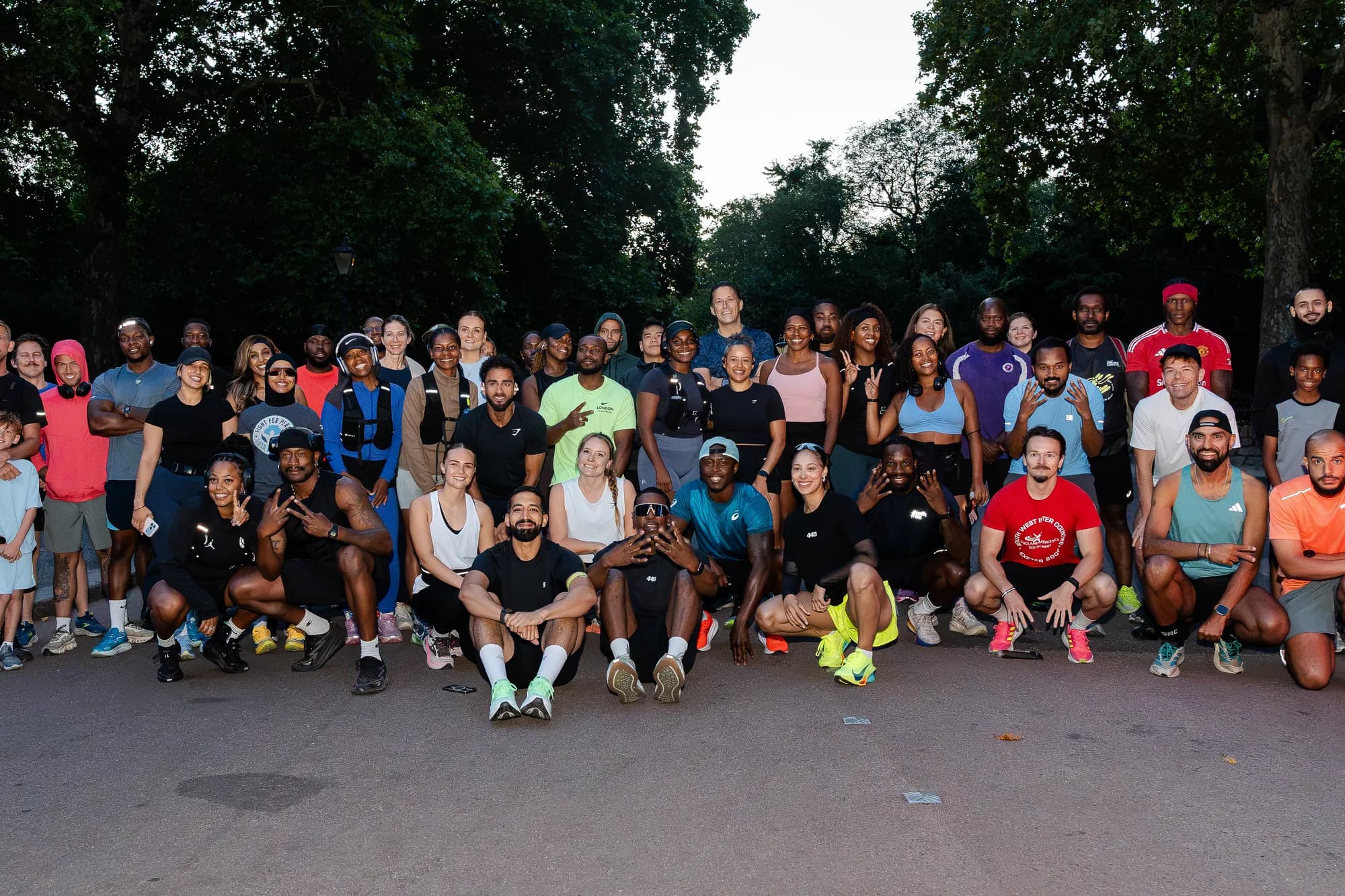 The full 445 Crew lined up across a park road at dusk, dozens of runners standing and crouching in front of the trees.