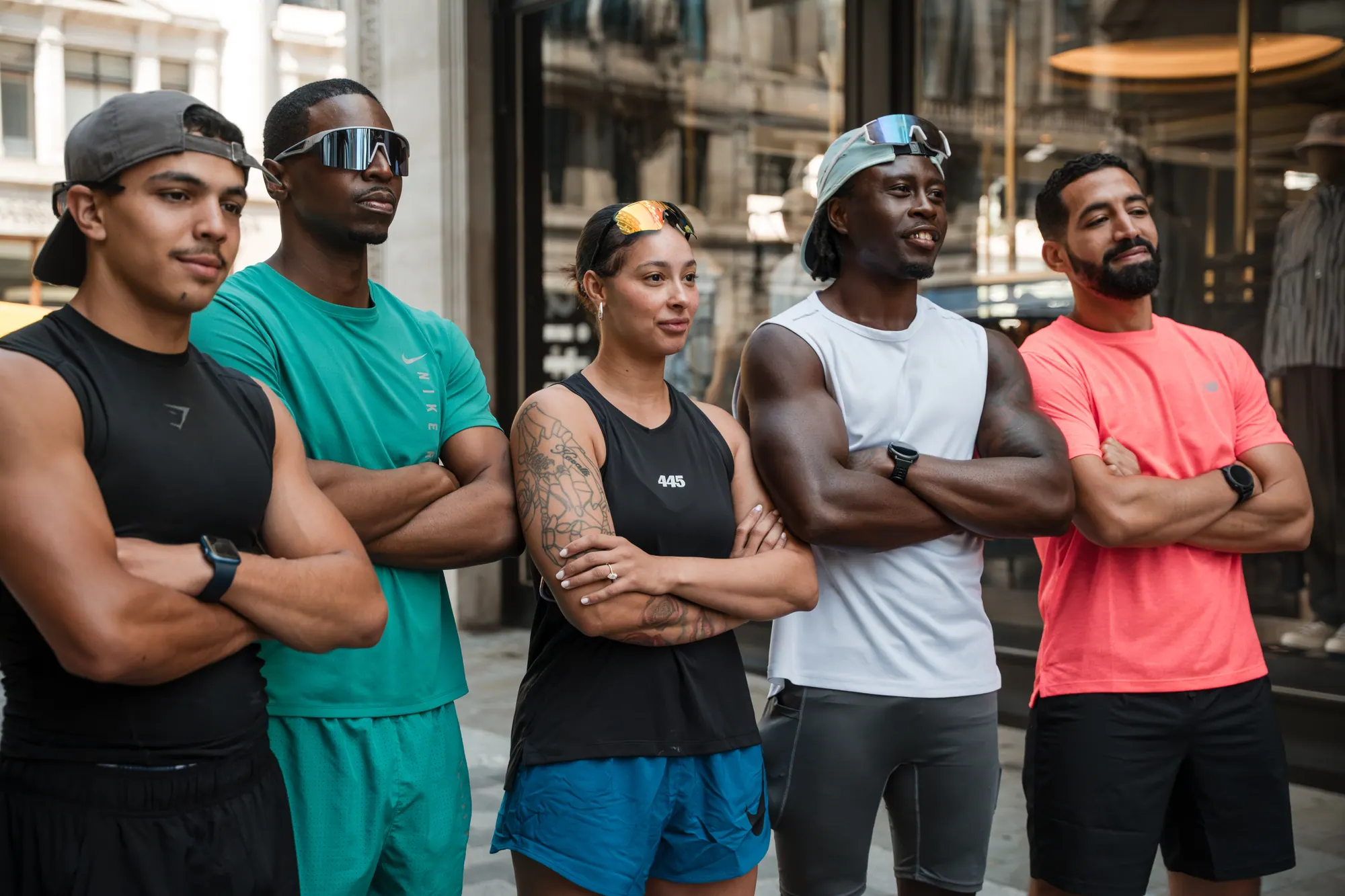Five runners standing in a line with arms crossed on a City of London street.