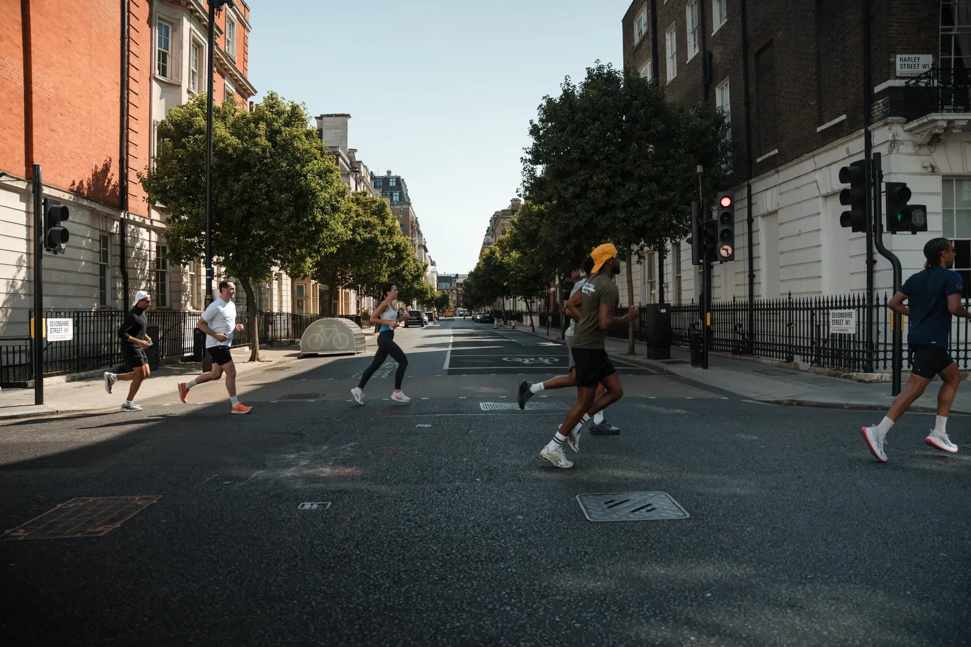 Six runners crossing an empty Harley Street in early morning light, strung out across the junction between Georgian terraces.