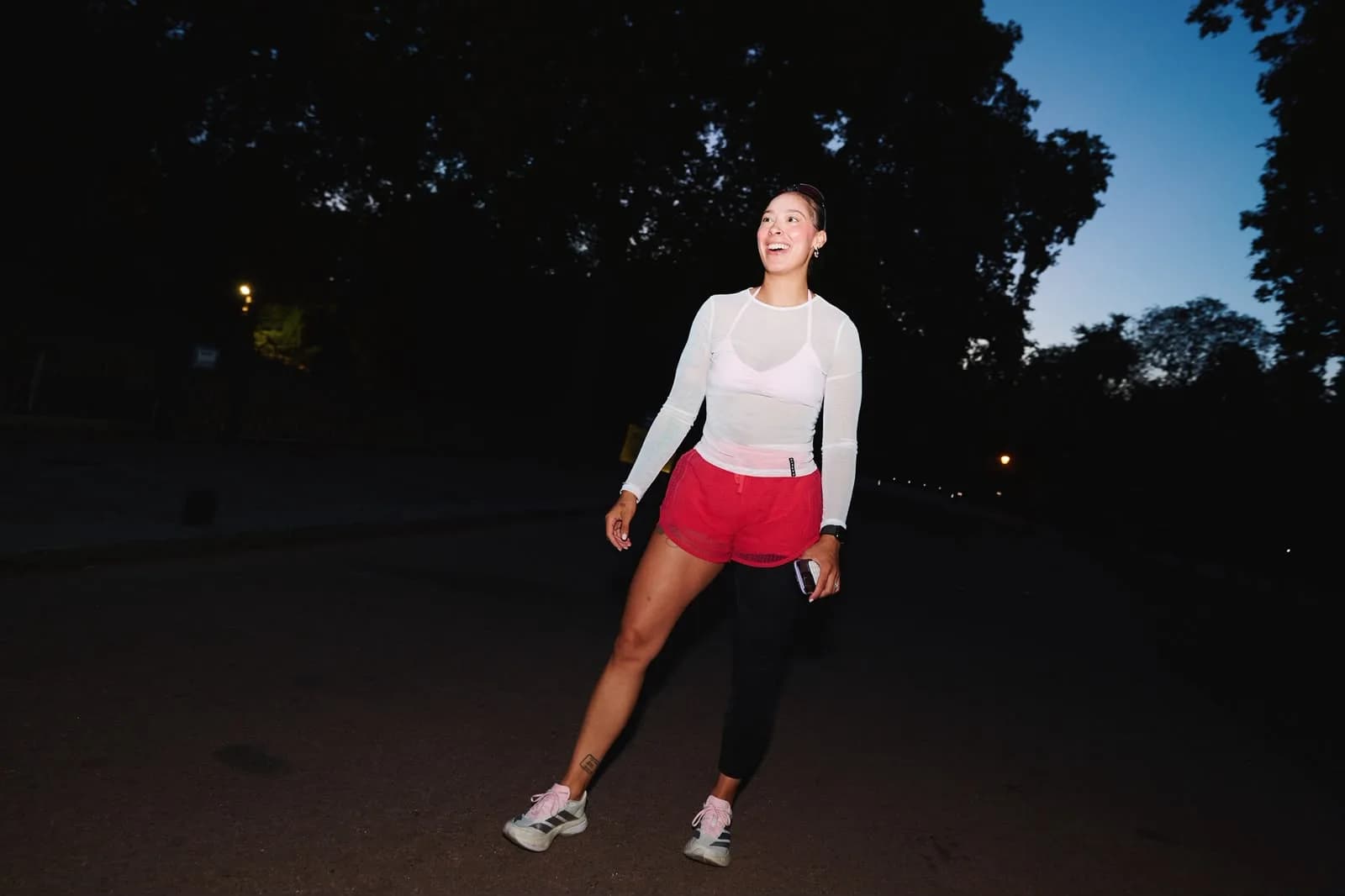Charlotte standing alone on an empty park road at dusk, laughing, in running kit.