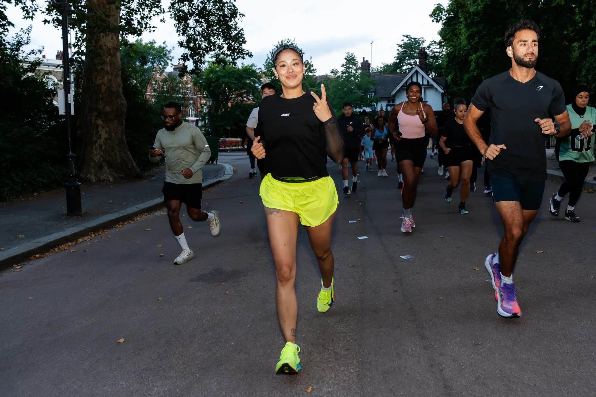 Charlotte leading a pack of 445 runners down a park road, throwing a peace sign, with the rest of the crew spread out behind her.